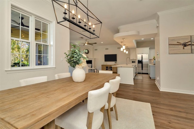 dining space with a fireplace, wood finished floors, a ceiling fan, baseboards, and crown molding