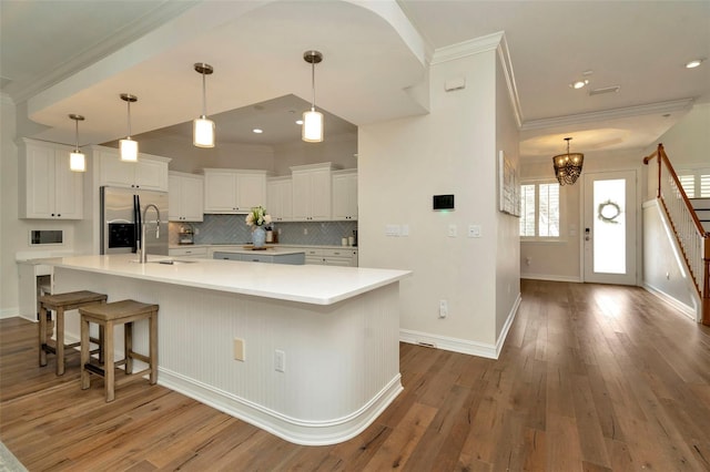 kitchen with ornamental molding, white cabinets, a sink, stainless steel fridge, and hardwood / wood-style flooring