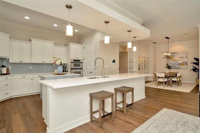 kitchen with light wood finished floors, stainless steel double oven, a sink, and a kitchen island with sink