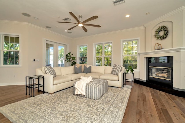 living area with visible vents, a glass covered fireplace, wood finished floors, and ornamental molding