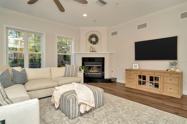 living room featuring ornamental molding, visible vents, baseboards, and wood finished floors