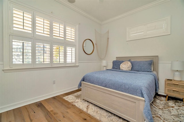 bedroom featuring a wainscoted wall, crown molding, baseboards, and wood finished floors