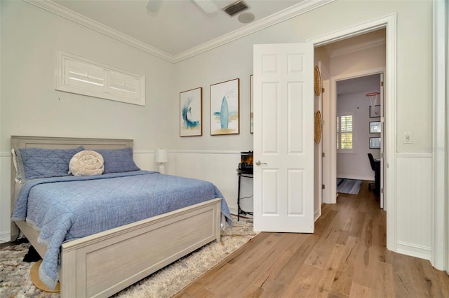 bedroom with a wainscoted wall, visible vents, ornamental molding, a ceiling fan, and wood finished floors