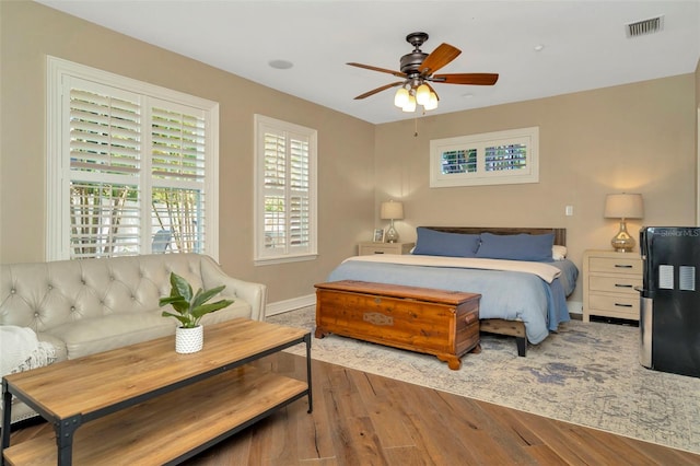 bedroom with a ceiling fan, wood finished floors, visible vents, and baseboards