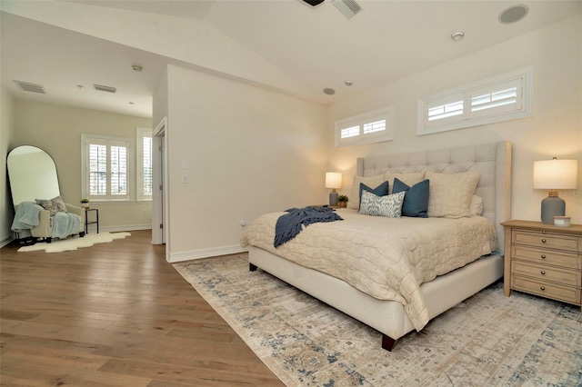 bedroom with multiple windows, visible vents, vaulted ceiling, and wood finished floors