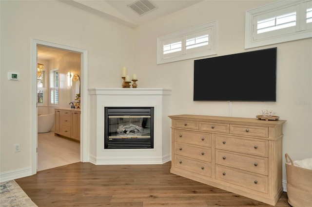 living area featuring visible vents, wood finished floors, and a glass covered fireplace