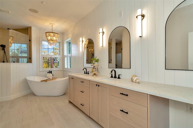 bathroom with a freestanding tub, a notable chandelier, wood finished floors, visible vents, and vanity