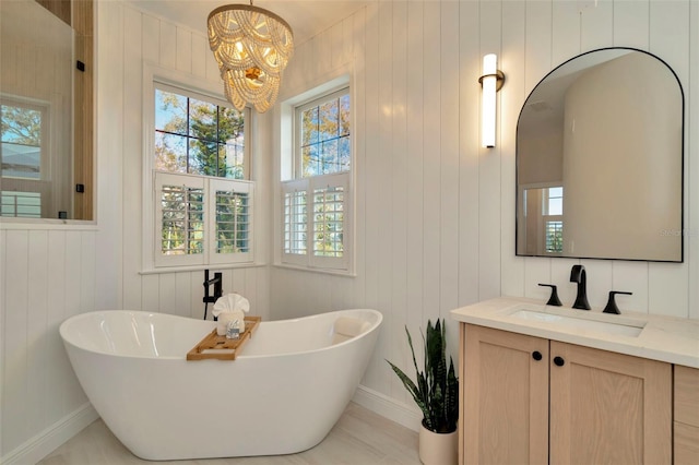 full bath with a chandelier, a soaking tub, vanity, and baseboards