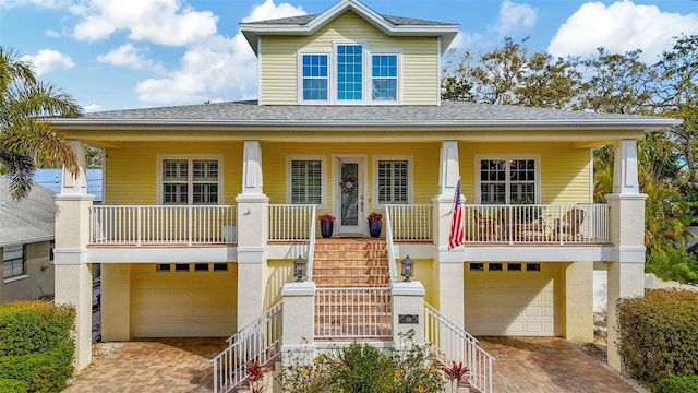 coastal inspired home featuring a porch, decorative driveway, an attached garage, and stairs