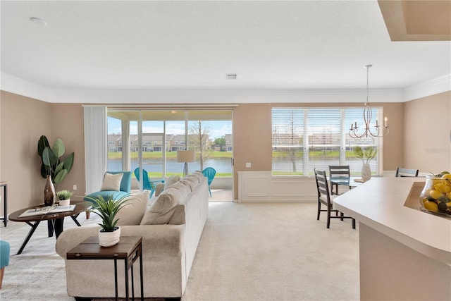 living area with visible vents, light carpet, an inviting chandelier, and ornamental molding