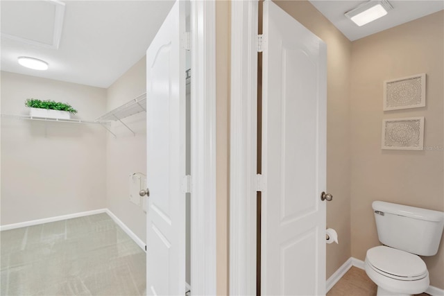 bathroom featuring toilet, a walk in closet, and baseboards