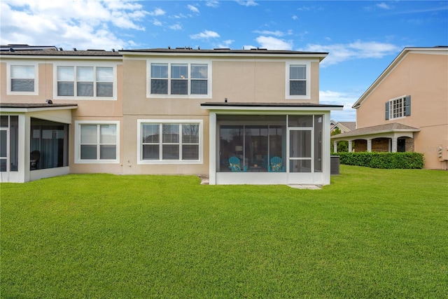 rear view of house with a lawn, a sunroom, and stucco siding