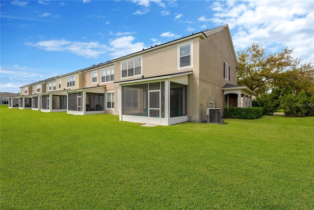 rear view of property with a yard, central AC unit, a sunroom, and stucco siding