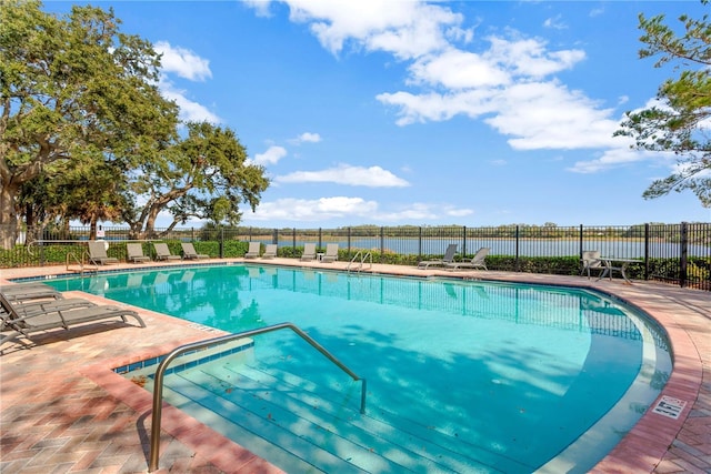 community pool with a water view, a patio, and fence