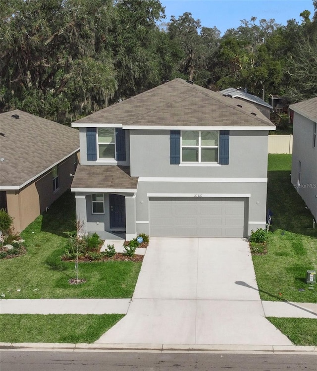 traditional home with an attached garage, concrete driveway, roof with shingles, stucco siding, and a front yard