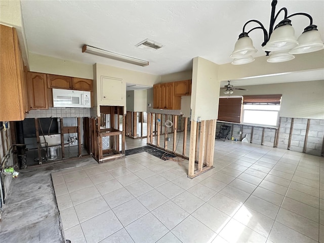 kitchen featuring light tile patterned floors, white microwave, visible vents, a ceiling fan, and brown cabinetry