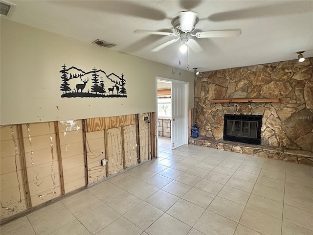 unfurnished living room with light tile patterned flooring, visible vents, a ceiling fan, and a stone fireplace