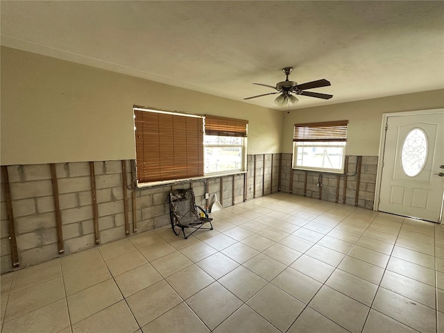 foyer entrance with a wainscoted wall, ceiling fan, light tile patterned floors, and tile walls