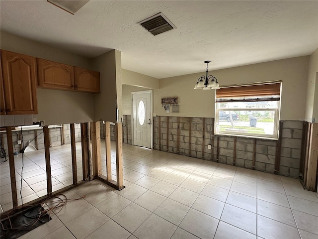 interior space featuring light tile patterned flooring, visible vents, a textured ceiling, and an inviting chandelier