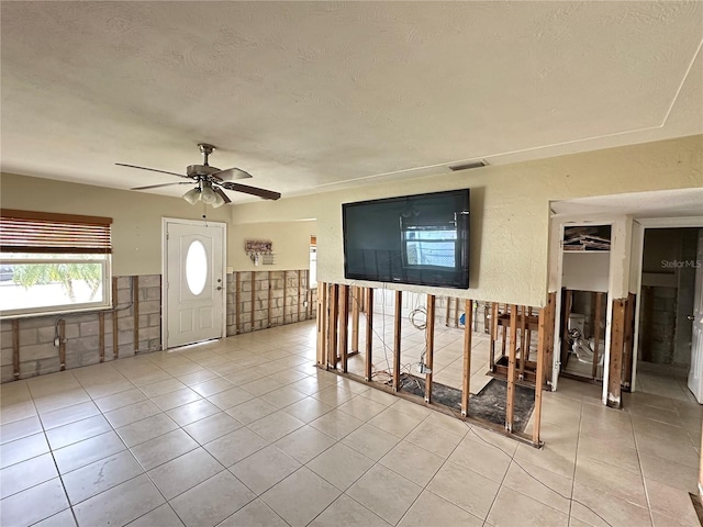 foyer featuring light tile patterned floors, visible vents, a textured wall, ceiling fan, and a textured ceiling