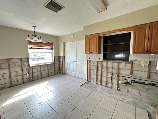 kitchen with light tile patterned floors, a textured ceiling, visible vents, hanging light fixtures, and brown cabinets