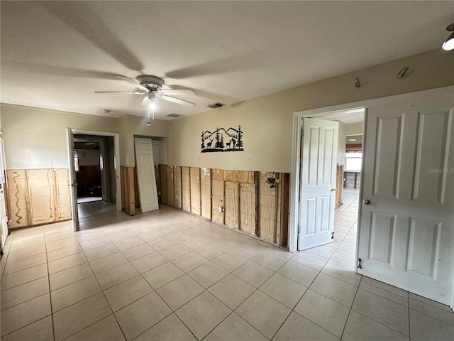 unfurnished room with light tile patterned floors, visible vents, wainscoting, and a ceiling fan