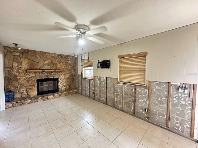 interior space with a ceiling fan, a fireplace, a textured ceiling, and light tile patterned floors