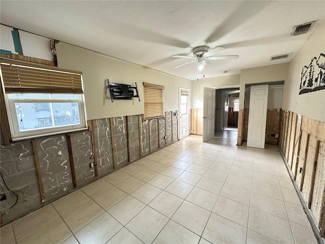 unfurnished room featuring a textured ceiling, light tile patterned flooring, visible vents, and a ceiling fan