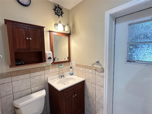 bathroom with toilet, a wainscoted wall, vanity, and tile walls