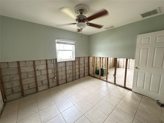 spare room featuring tile walls, visible vents, a ceiling fan, and light tile patterned flooring