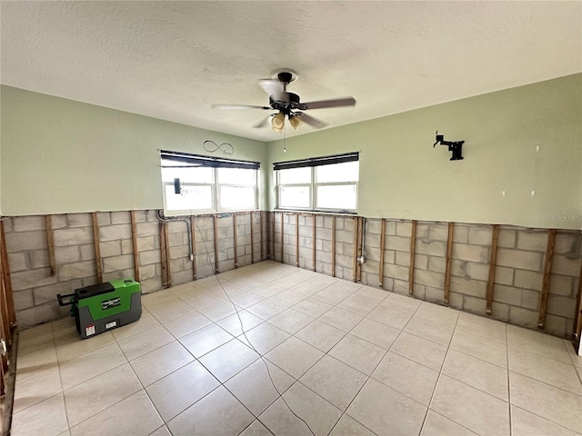 unfurnished room featuring a wainscoted wall, ceiling fan, a textured ceiling, and light tile patterned floors