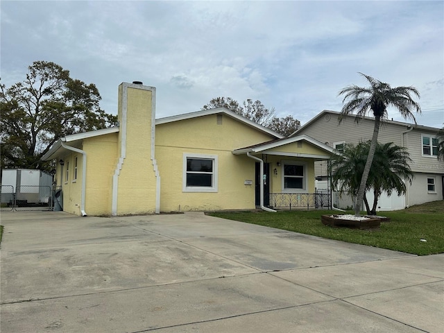 view of front of home featuring covered porch, driveway, stucco siding, a front lawn, and a chimney