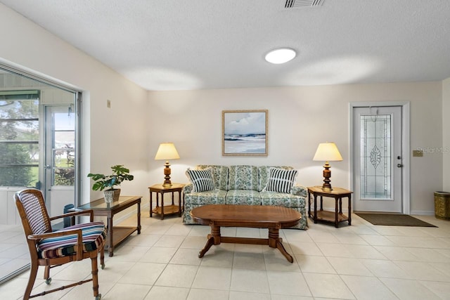 living area featuring light tile patterned floors, visible vents, baseboards, and a textured ceiling