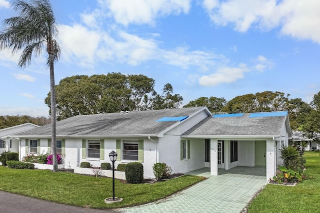 ranch-style home with stucco siding, roof with shingles, decorative driveway, and a front yard