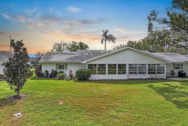 back of property at dusk featuring a sunroom and a lawn