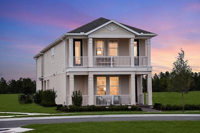 view of front of home with a balcony, covered porch, stucco siding, and a front yard