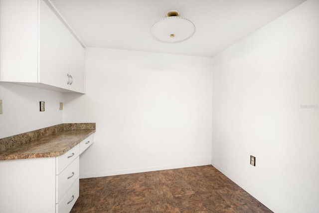 kitchen with stone finish floor, white cabinets, baseboards, and built in study area