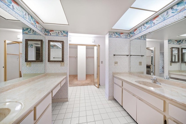 full bathroom featuring a skylight, two vanities, a sink, and wallpapered walls