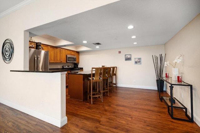 kitchen with visible vents, brown cabinetry, dark countertops, appliances with stainless steel finishes, and a breakfast bar area