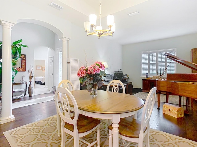 dining space featuring arched walkways, visible vents, dark wood-type flooring, a chandelier, and ornate columns