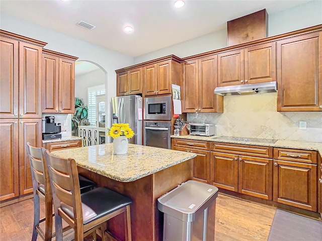 kitchen with stainless steel appliances, brown cabinets, under cabinet range hood, and a kitchen bar