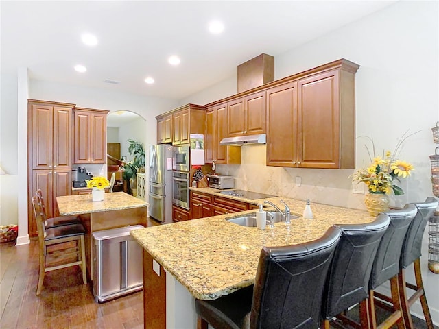 kitchen featuring arched walkways, a peninsula, a kitchen island, a sink, and a kitchen breakfast bar