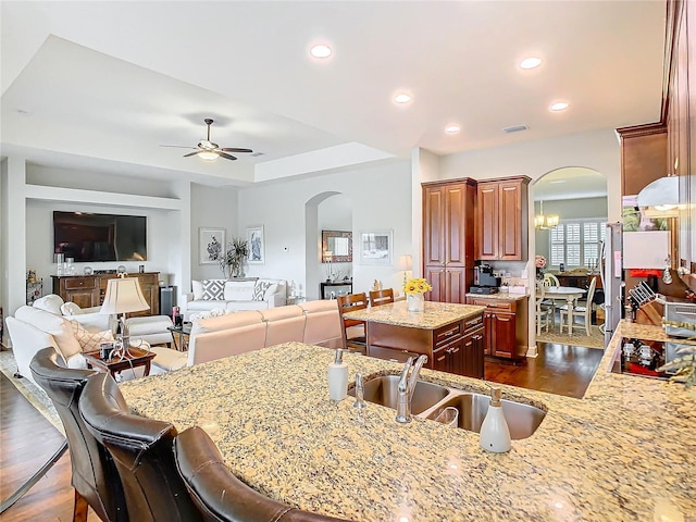 kitchen with arched walkways, a kitchen island, open floor plan, a kitchen bar, and a sink