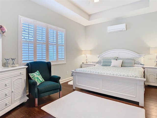 bedroom featuring dark wood-style floors, baseboards, a tray ceiling, and a wall mounted air conditioner