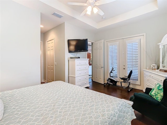 bedroom with ceiling fan, visible vents, dark wood-type flooring, and a tray ceiling