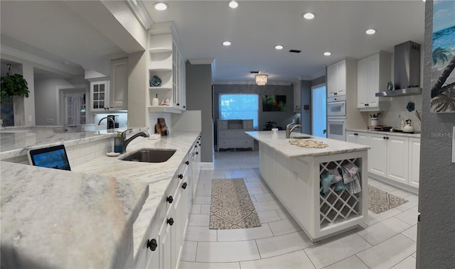 kitchen with open shelves, double oven, light stone counters, wall chimney exhaust hood, and a sink