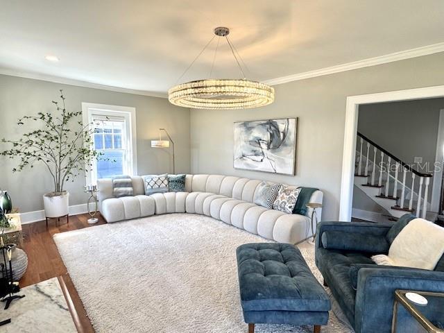 living room with baseboards, stairway, an inviting chandelier, dark wood finished floors, and crown molding