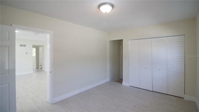 unfurnished bedroom featuring visible vents, a closet, light wood-style flooring, and baseboards