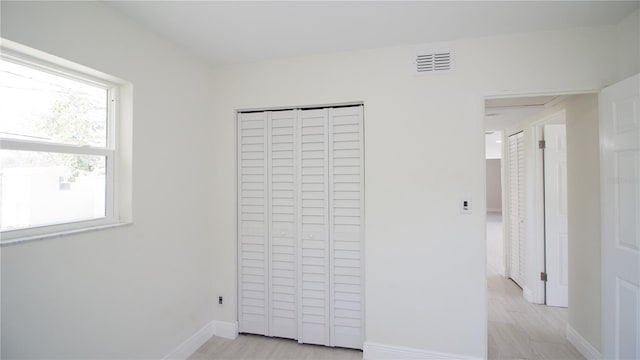 unfurnished bedroom with baseboards, light wood-style flooring, visible vents, and a closet