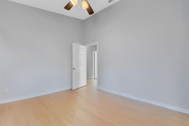 spare room featuring a towering ceiling, light wood finished floors, baseboards, and a ceiling fan